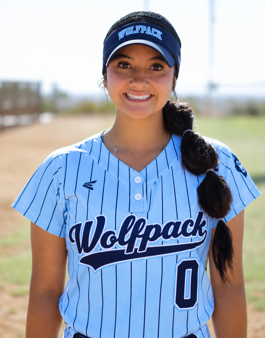 Rae Gaitan wearing her light-blue Wolfpack number 0 jersey and navy WOLFPACK visor at a softball field